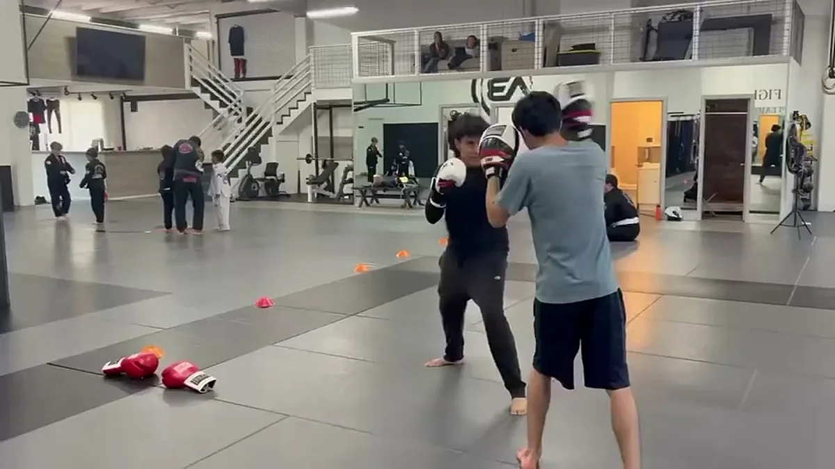 Students practicing boxing mitt work while a kids martial arts class trains in the background at AB MMA in Portola, San Francisco