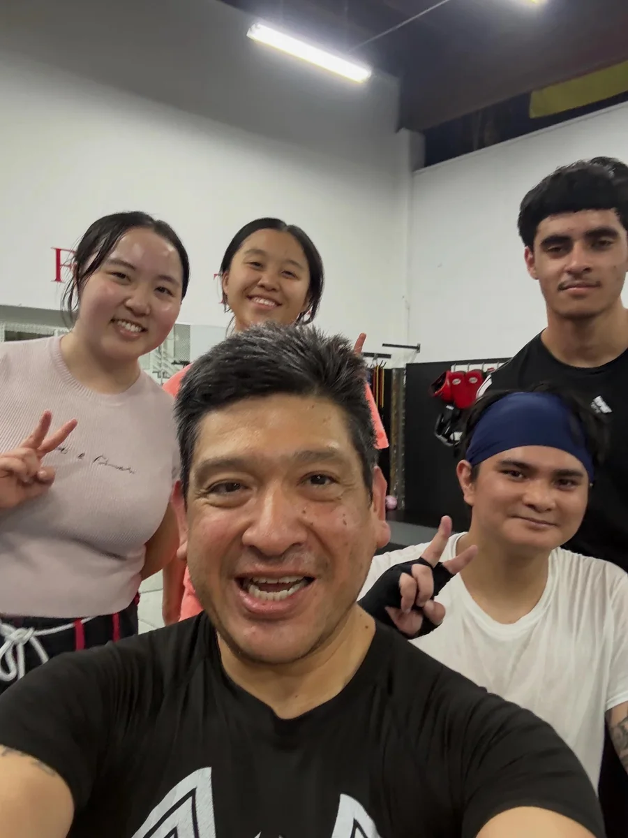 Coach and adult students smiling and making peace signs after a Muay Thai class at AB MMA on San Bruno Avenue